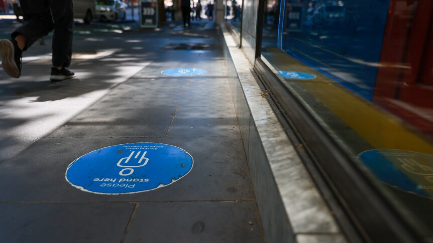 Faded social distance stickers on the footpath and people walking with masks as they pass hand sanitiser stations.