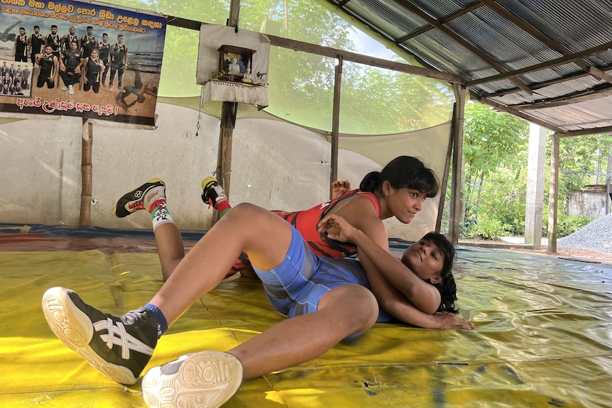 Two female wrestlers are training, one has the other pinned to the mat.