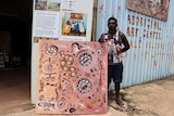 an Indigenous man holds a painting outside an art centre