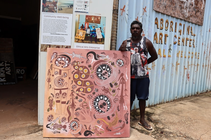 an Indigenous man holds a painting outside an art centre