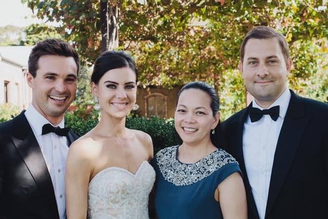 Two men and two women smile for a photo one of the women is a bride in a wedding a dress