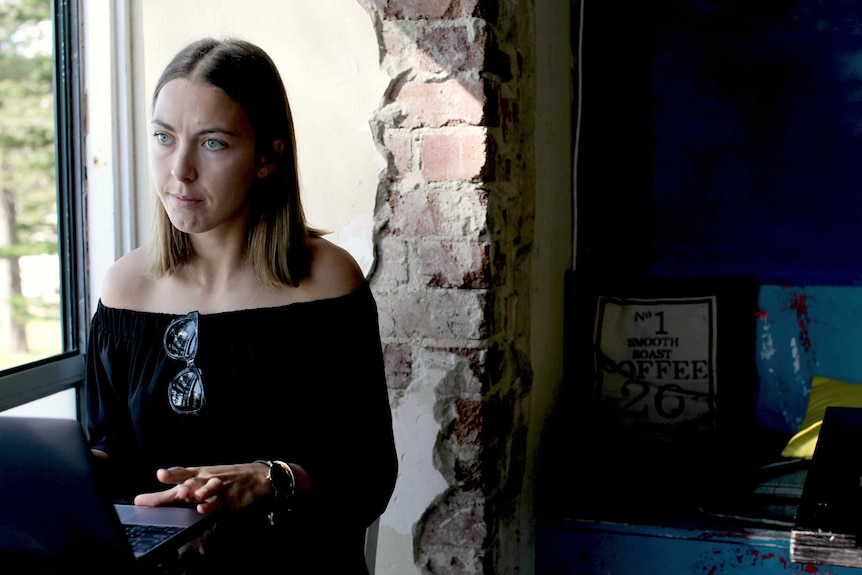 Alice Pritchard Davies sits at a table in a cafe looking into the distance