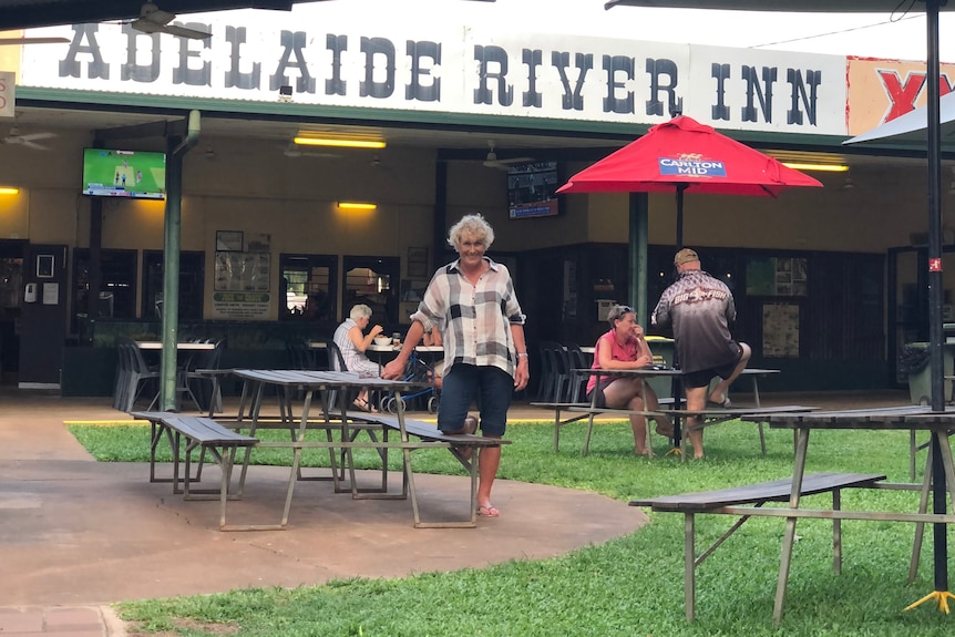 Woman wearing shorts and shirt, smiling, standing in a beer garden outside pub called Adelaide River Inn.