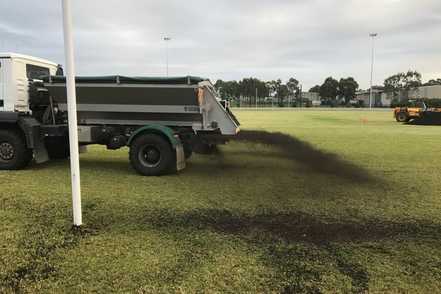 Black soil falling out of the back of a truck on a football field.
