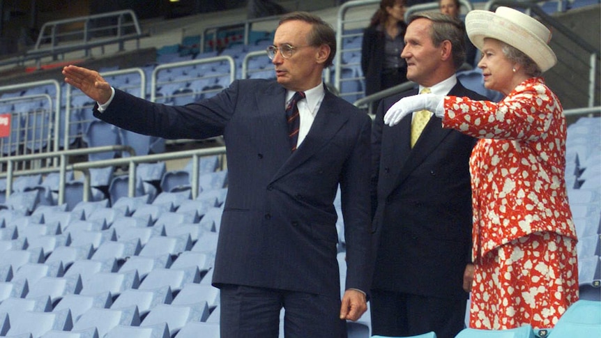 Queen Elizabeth II watches as Bob Carr points inside a Sydney stadium.