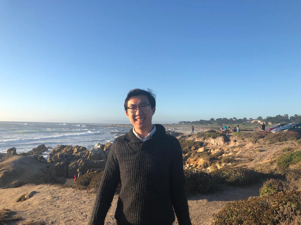 A young man standing on a beach with sea in the background