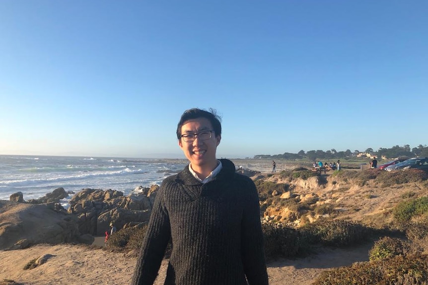 A young man standing on a beach with sea in the background