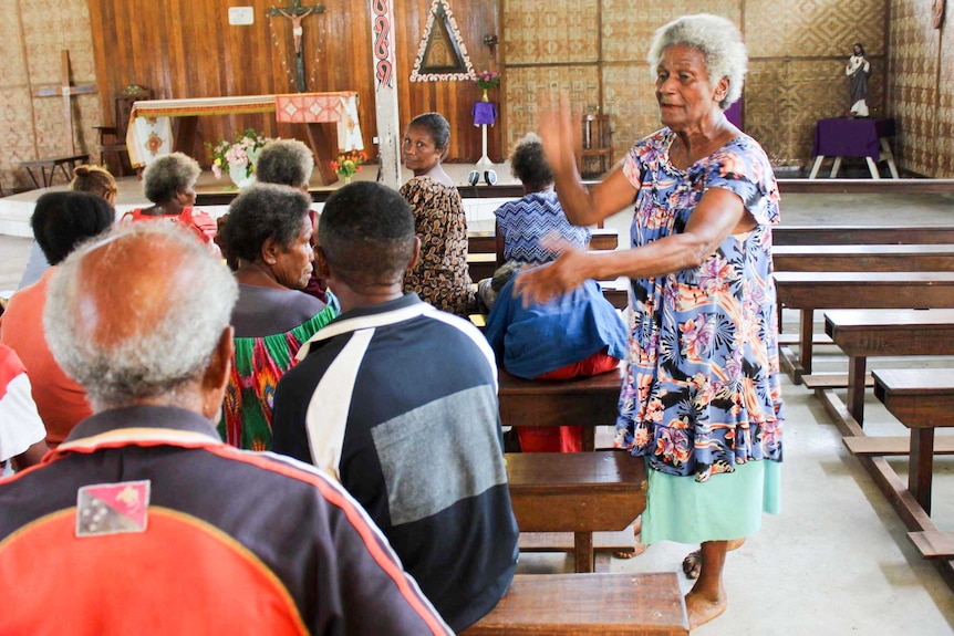 An older woman leads a choir in a church on an island in Papua New Guinea.