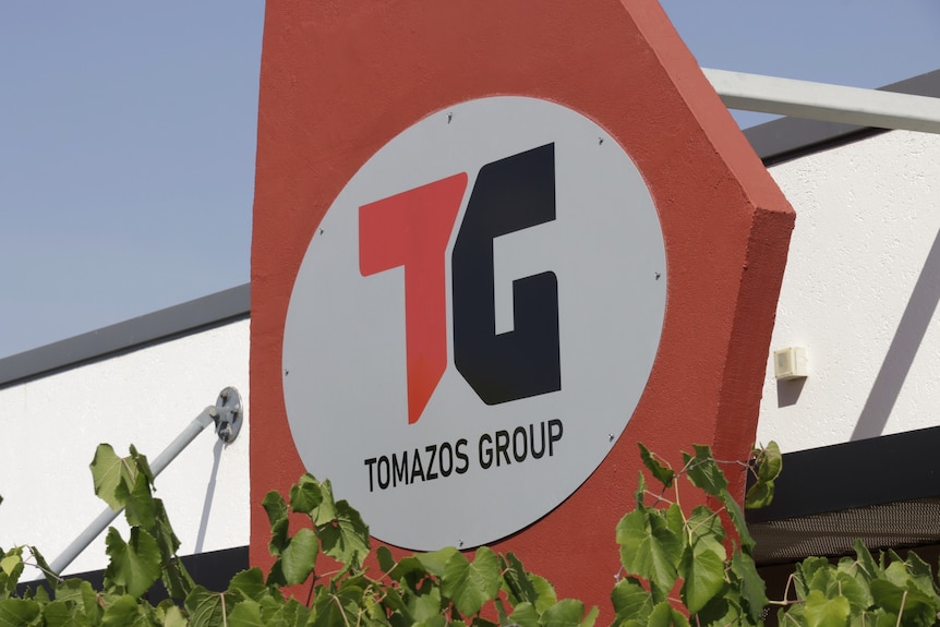 A red sign with the letters 'TG' and the words 'Tomazos Group' on the side of an industrial building.