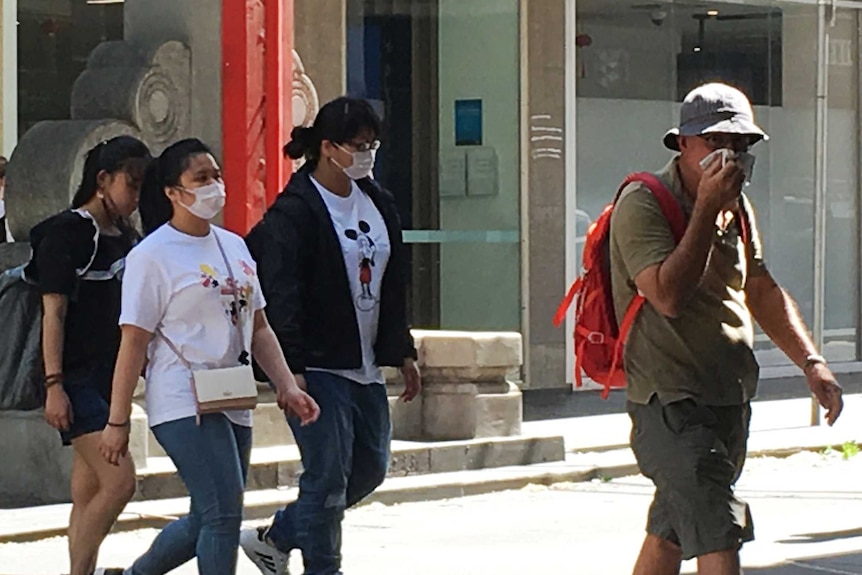 Pedestrians wearing masks cross a Melbourne intersection.