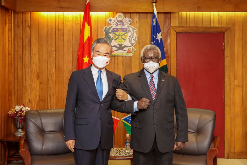 Wang Yi and Manasseh Sogavare lock arms while posing for a photo in a timber-clad office.