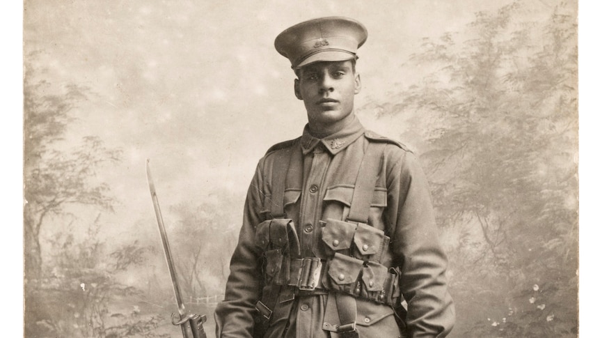 An old black-and-white photo of a man in military uniform standing in a photography studio.