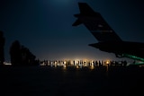 Silhouette of a line of Afghans waiting to be boarded onto a military aircraft in the dark.