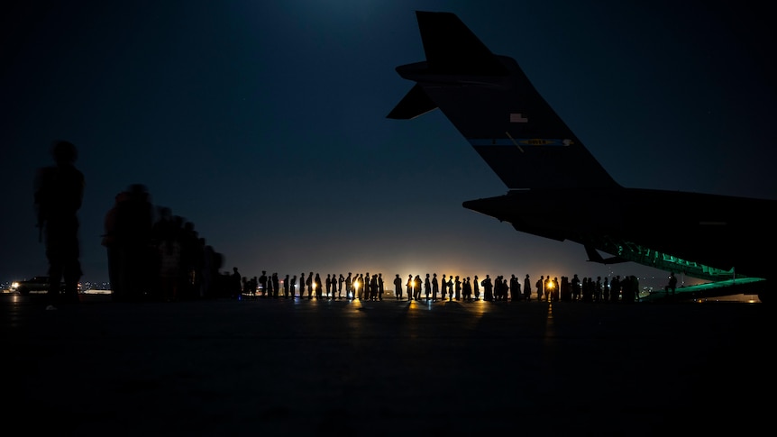 Silhouette of a line of Afghans waiting to be boarded onto a military aircraft in the dark.