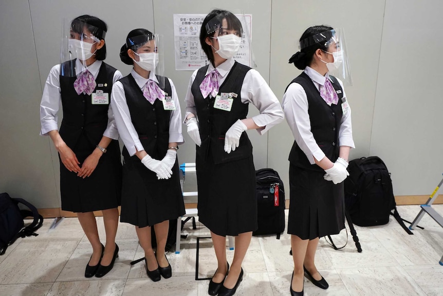 Four women in matching skirt suits, face masks and clear plastic face shields