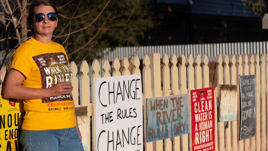 Bourke resident Fleur Thompson stands next to a fence covered in placards calling for clean drinking water.