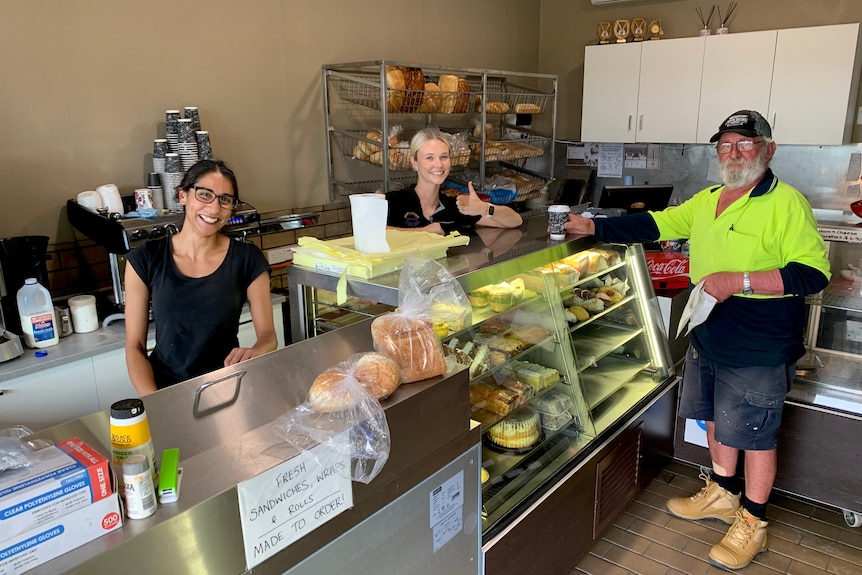 The interior of a bakery with two people behind the counter and one customer buying a coffee and baked items.