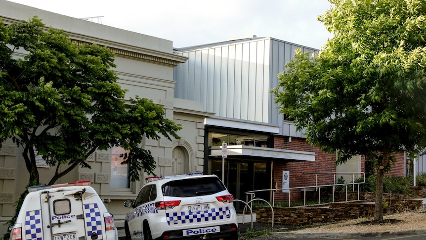 Street view of Castlemaine police station, with two police cars parked out front on a tree-lined street.