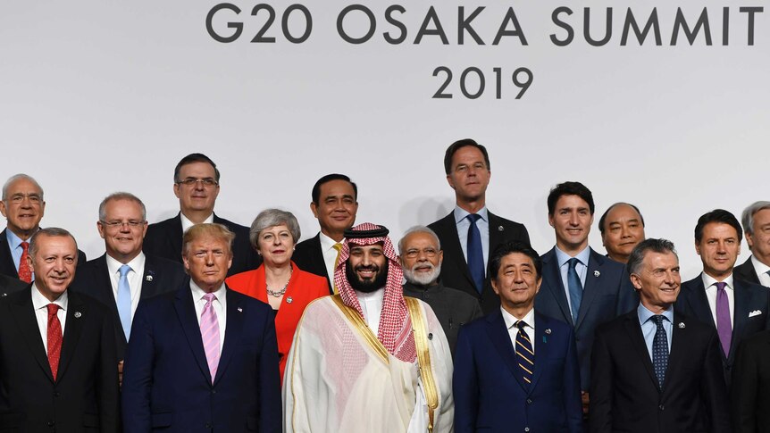 World leaders including Donald Trump, Theresa May, and Shinzo Abe stand on a podium for a group photo