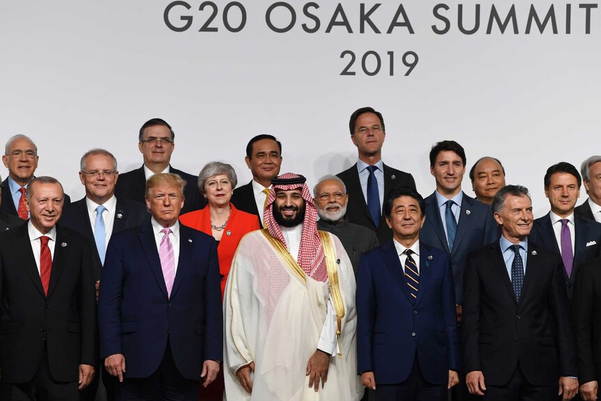 World leaders including Donald Trump, Theresa May, and Shinzo Abe stand on a podium for a group photo