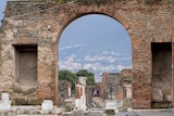 Brick archway to an Italian archaeological site, with people in the distance waling through.