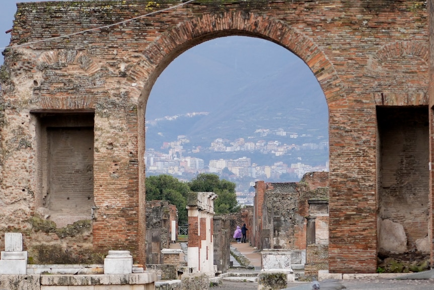 Brick archway to an Italian archaeological site, with people in the distance waling through.