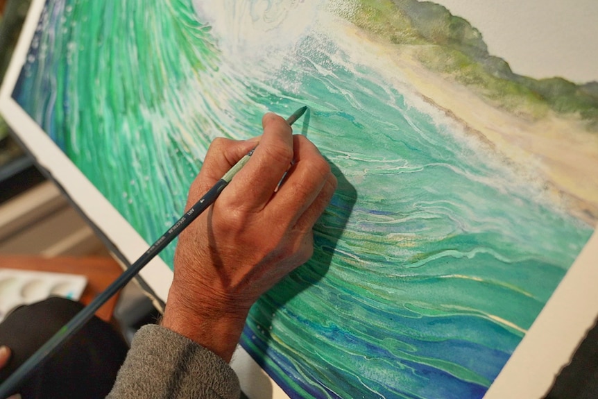 Colin's hand with a paintbrush paints a wave.