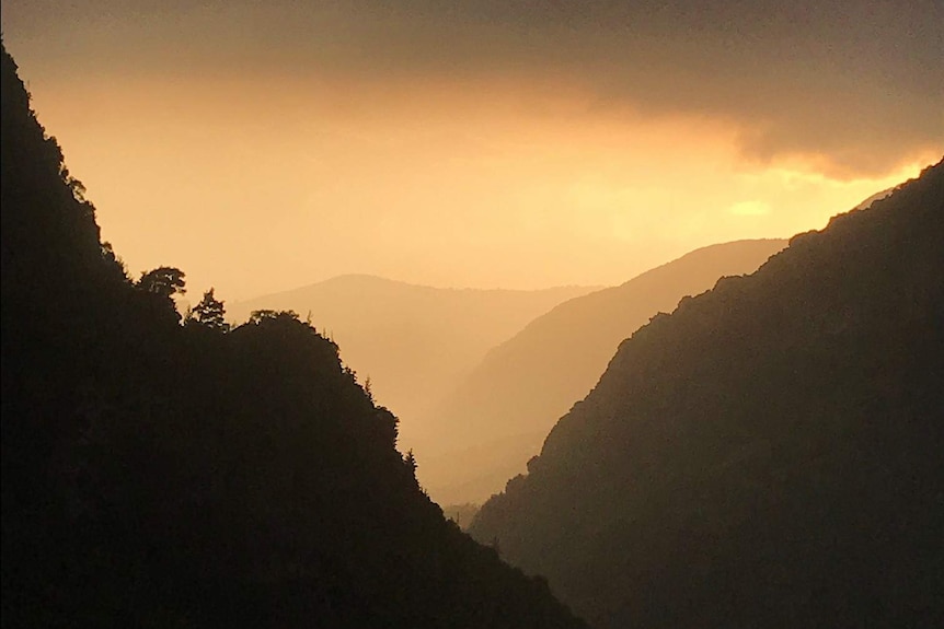The sunset turns the sky orange against the mountains of Lebanon's Qadisha Valley.