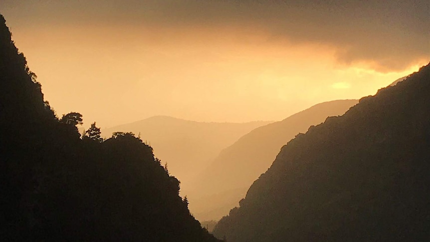 The sunset turns the sky orange against the mountains of Lebanon's Qadisha Valley.
