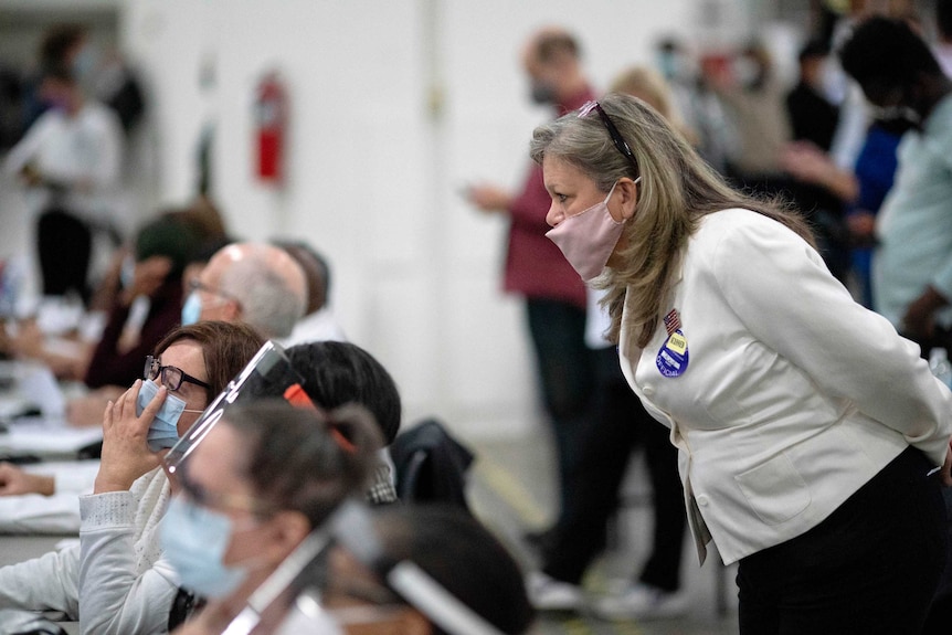 A Republican election challenger at right watches over election inspectors as they examine a ballot.