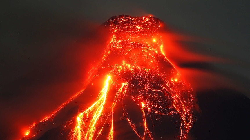 Glowing red molten lava spews from the top of Mayon volcano