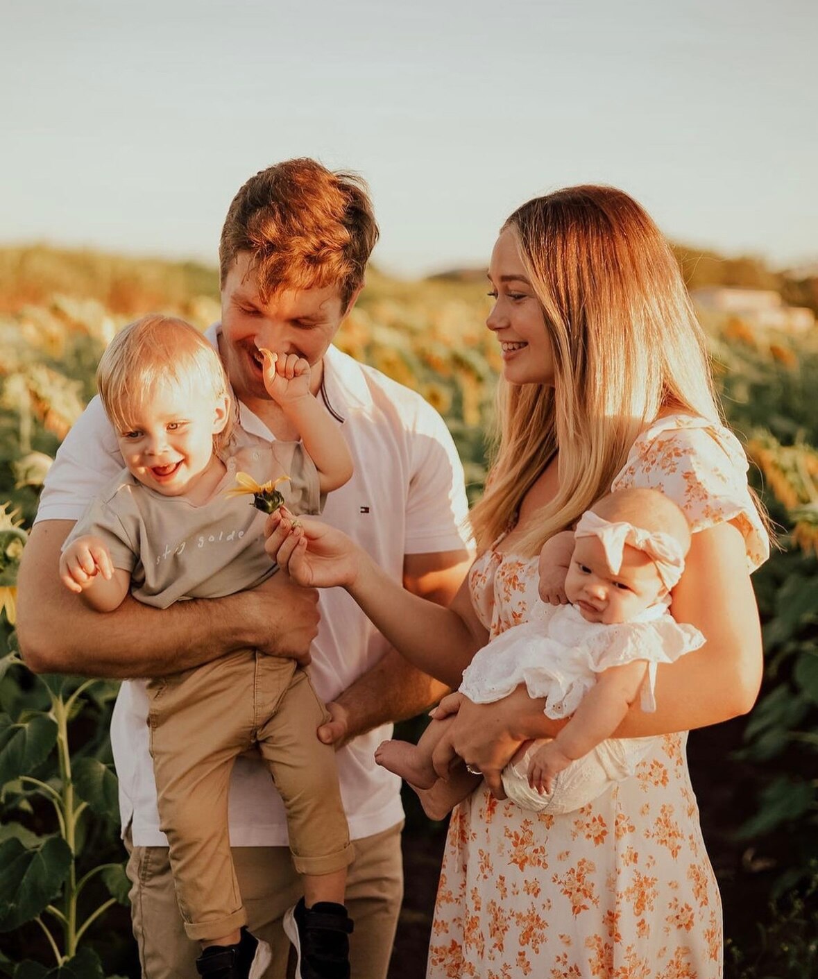 A young man and woman hold their toddler son and infant daughter in a grassy field that's drenched in golden hour sunlight.