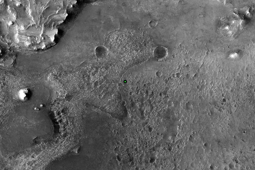High-resolution still image of the surface of Mars, with a green dot depicting where Perseverance landed.