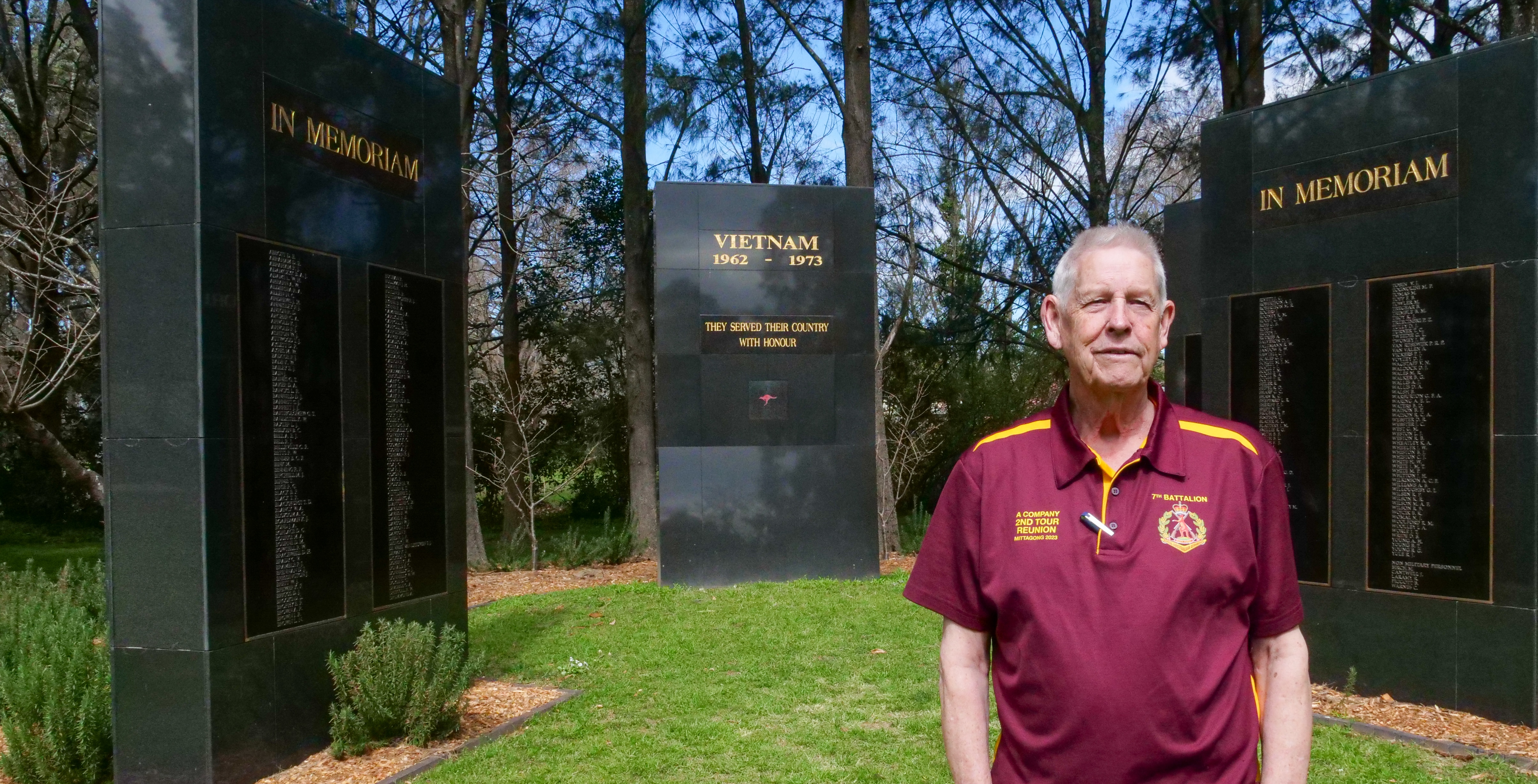 A Vietnam veteran stands in front of a war memorial in a park.
