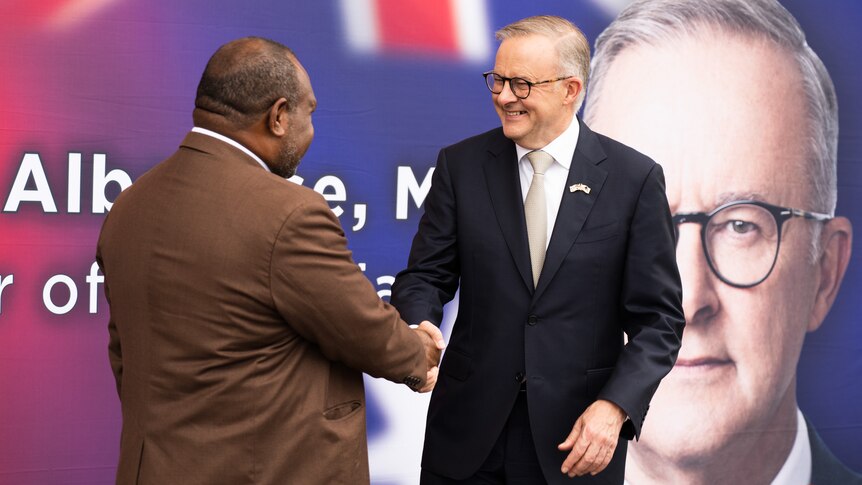 James Marape and Anthony Albanese stand and shake hands in front of a sign displaying the Australian leader's face.