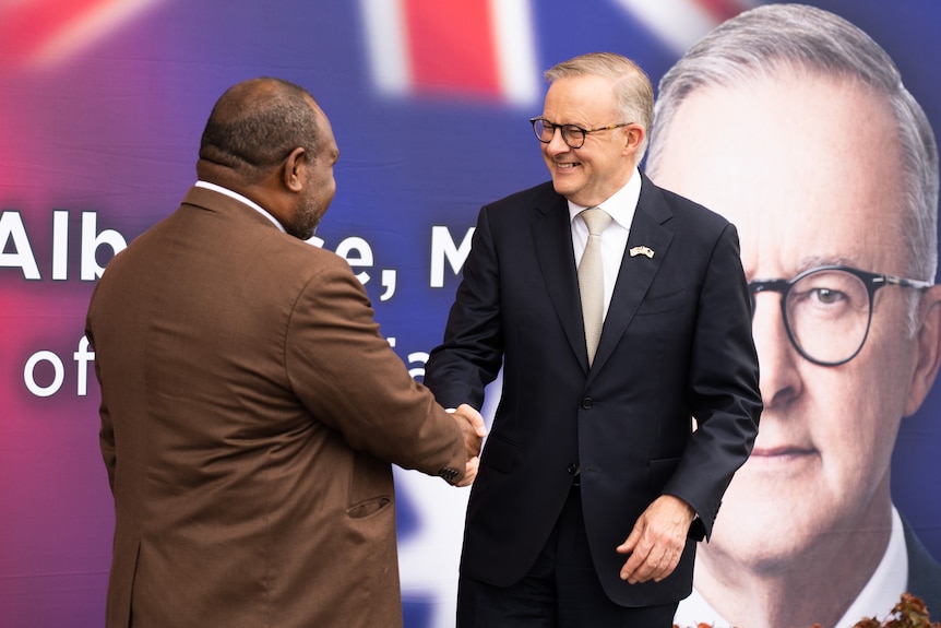 James Marape and Anthony Albanese stand and shake hands in front of a sign displaying the Australian leader's face.