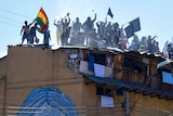 Men waving flags and banners on the roof of a dilapidated building.