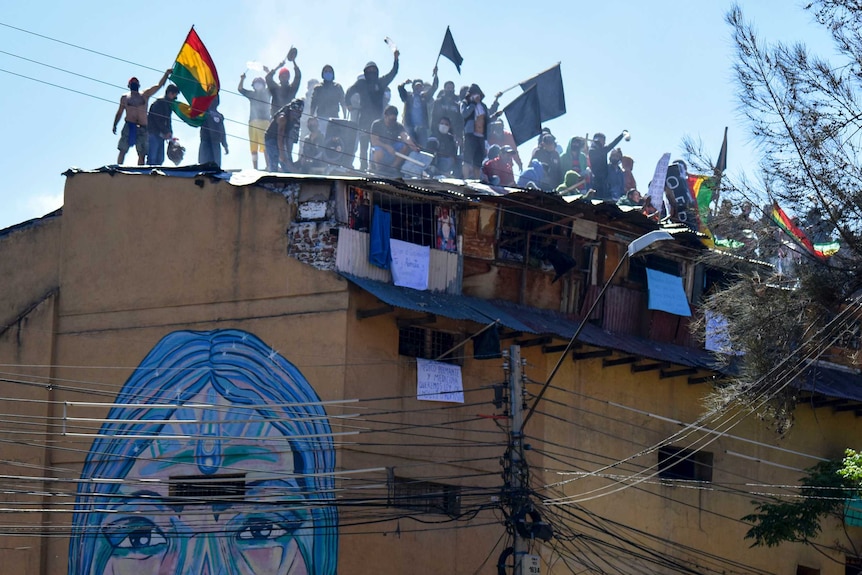 Men waving flags and banners on the roof of a dilapidated building.