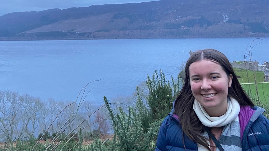 Lily stands in front of a picturesque backdrop of water and hills