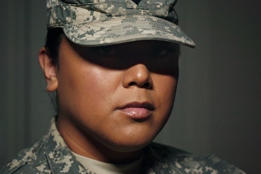 A woman in army fatigures with her cap shading her eyes