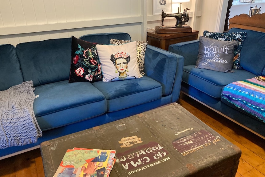 A lounge room decorated in 1940's style with a blue lounge, cushions and an old sewing machine and coffee table.