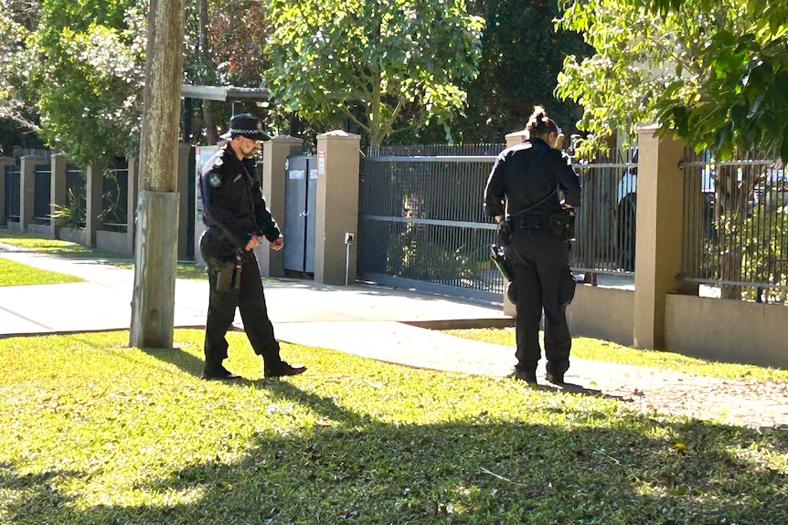 Two uniformed police officers examine a footpath outside a fenced unit complex