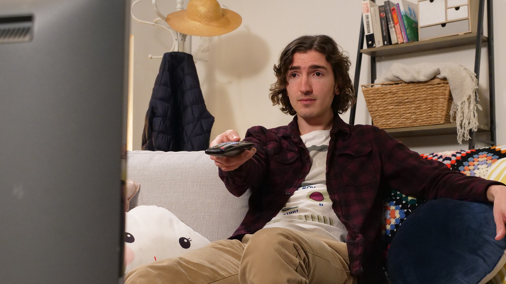 Thomas sits on a couch, pointing a remote at a television.