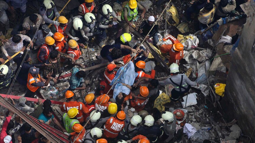 A bird's eye view sows a woman wrapped in a blue blanket on a stretcher sitting in the middle of a crowd of rescue workers.