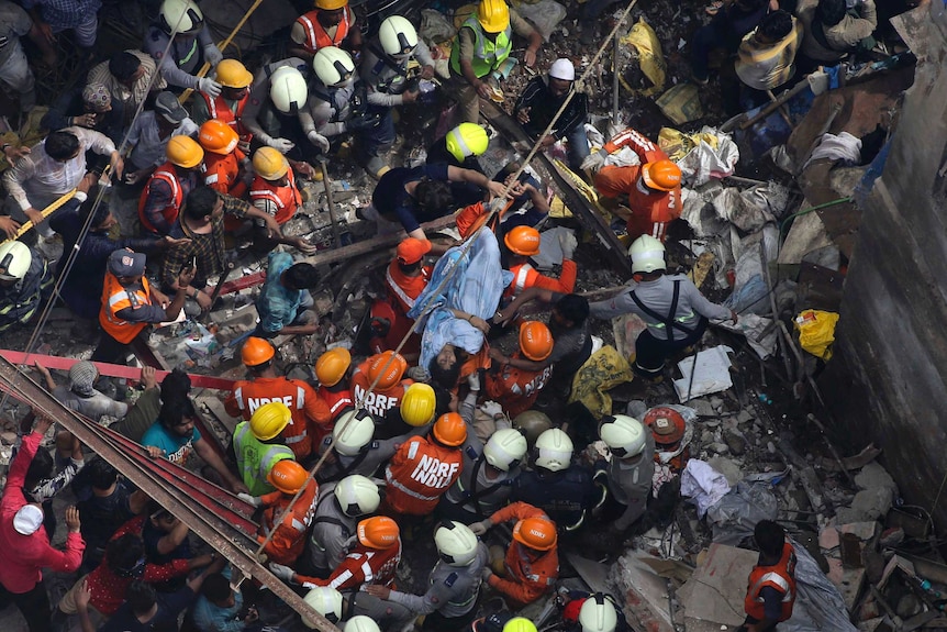 A bird's eye view sows a woman wrapped in a blue blanket on a stretcher sitting in the middle of a crowd of rescue workers.