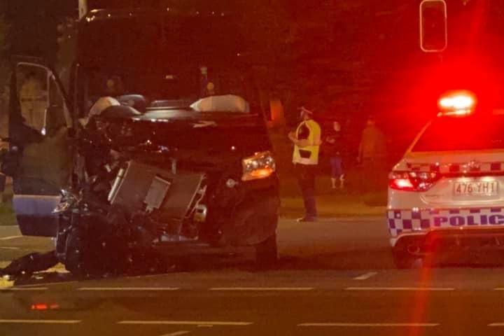 A smashed blue mini-van with a police car with sirens on.