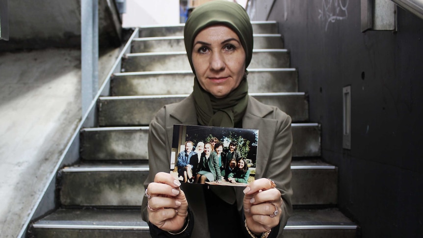 Profile photo of Halee Cosar sitting on stairs, holding a photo, looking down the camera.