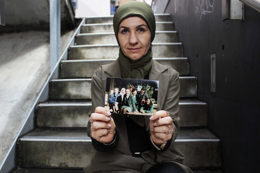 Profile photo of Halee Cosar sitting on stairs, holding a photo, looking down the camera.