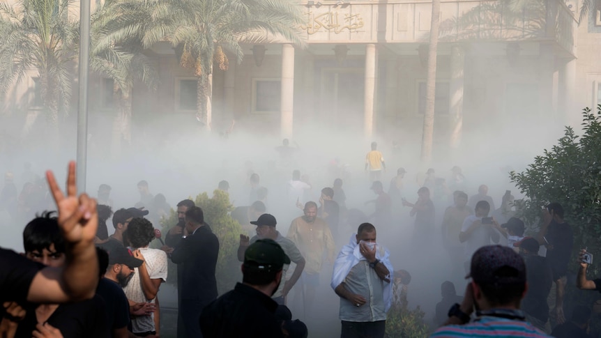 A man cover his face with a cloth as tear gas erupts around the crowd