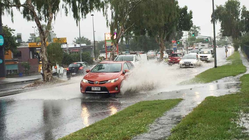 A car drives through heavy rain water at Fairfield Road in Yeronga.